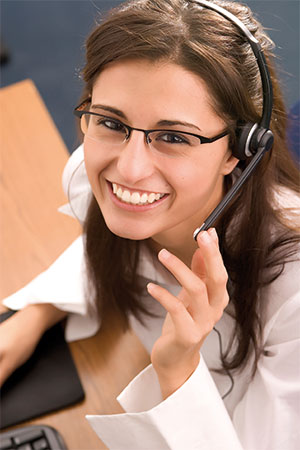 Frau mit braunen Haaren trägt Headset und weiße Bluse, sitzt an Schreibtisch mit Computermaus und Tastatur