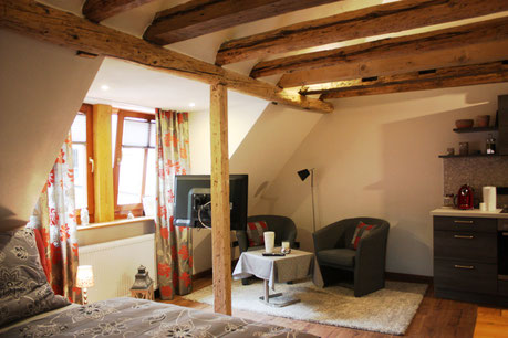 Dachstudio mit Holzbalken, Kuechenzeile, Sitzgecke und Doppelbett in Heppenheim.