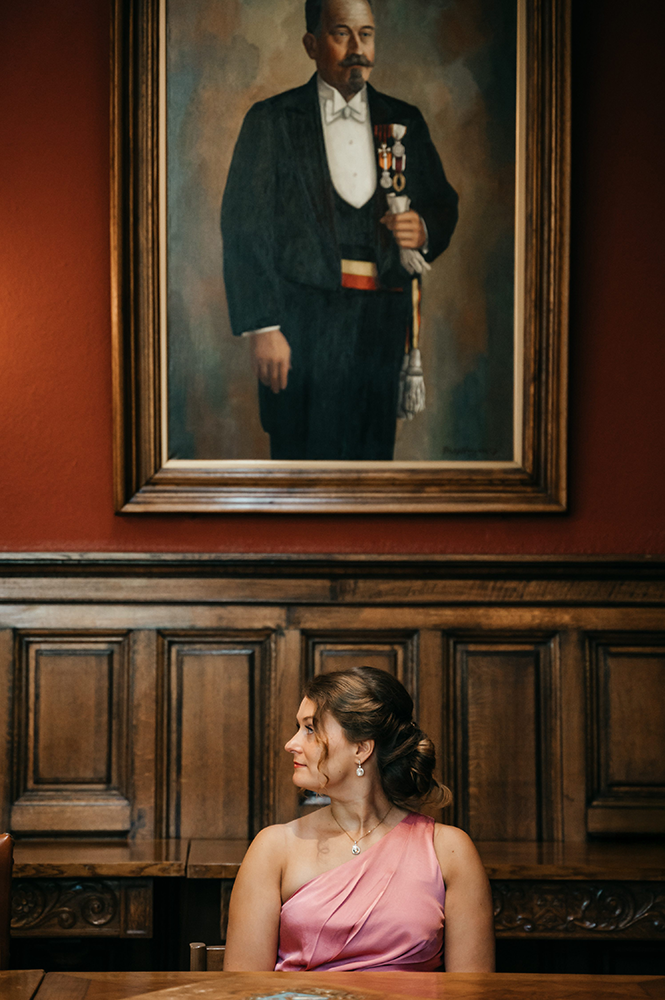 dame zit in het gemeentehuis net onder een staatsieportret, wat een grappige dynamiek aan het beeld geeft-huwelijksfotografie-trouwreportage-byFotografils-IlseWagemakers-Fotograaf gevestigd in Essen