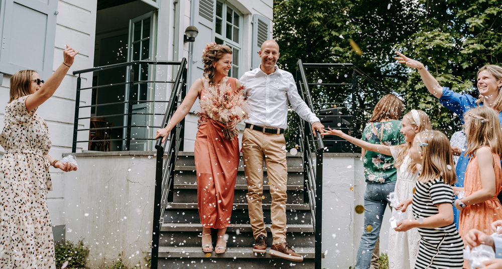 bruidspaar wandelt lachend af de trap terwijl de omstaanders confetti toewerpen-huwelijksfotografie-trouwreportage-byFotografils-IlseWagemakers-Essen