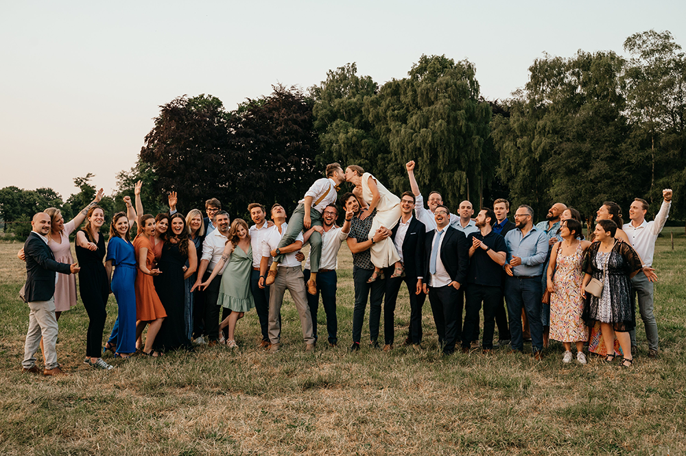 grote groepsfoto waarbij de bruid en de bruidegom op de schouders worden gedragen en ze elkaar zo kussen-huwelijksfotografie-trouwreportage-byFotografils-IlseWagemakers-Fotograaf gevestigd in Essen