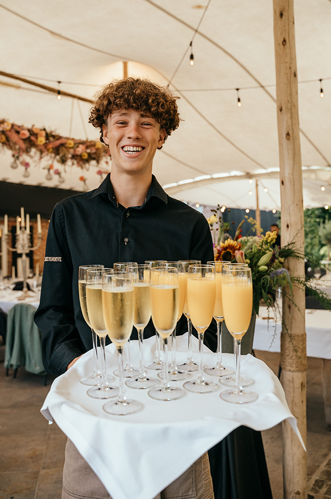 kelner presenteert al lachend cava en fruitsap-huwelijksfotografie-trouwreportage-byFotografils-IlseWagemakers-Fotograaf gevestigd in Essen