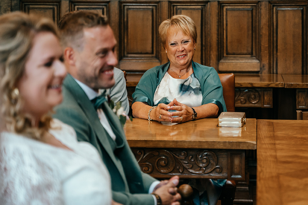 moeder van de bruidegom kijkt vol trots naar het paar tijdens de burgerlijke plechtigheid-huwelijksfotografie-trouwreportage-byFotografils-IlseWagemakers-Fotograaf gevestigd in Essen