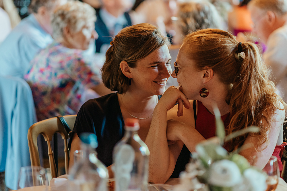 twee dames kijken elkaar liefkozend aan gezeten aan de feesttafel-huwelijksfotografie-trouwreportage-byFotografils-IlseWagemakers-Fotograaf gevestigd in Essen