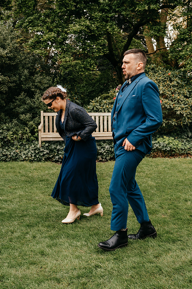 gasten van het huwelijk wandelen grappig doorheen het natte gras; ze houden daarbij hun kleren omhoog om ze te beschermen-huwelijksfotografie-trouwreportage-byFotografils-IlseWagemakers-Fotograaf gevestigd in Essen