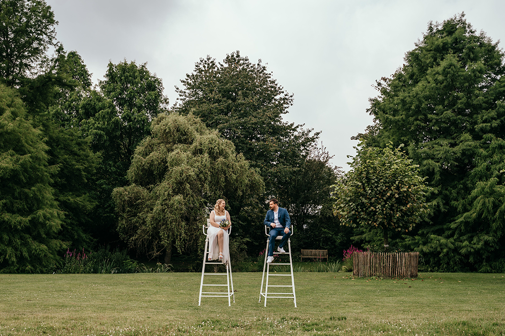 bruid en bruidegom poseren beide zittend in een hoge scheidsrechterstoel, midden in het groen van het Arboretum-huwelijksfotografie-trouwreportage-byFotografils-IlseWagemakers-Fotograaf gevestigd in Essen