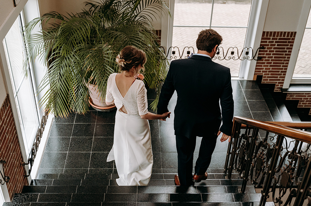 bruidegom en bruid wandelen af de trappen van het gemeentehuis, foto genomen op de rug-huwelijksfotografie-trouwreportage-byFotografils-IlseWagemakers-Fotograaf gevestigd in Essen
