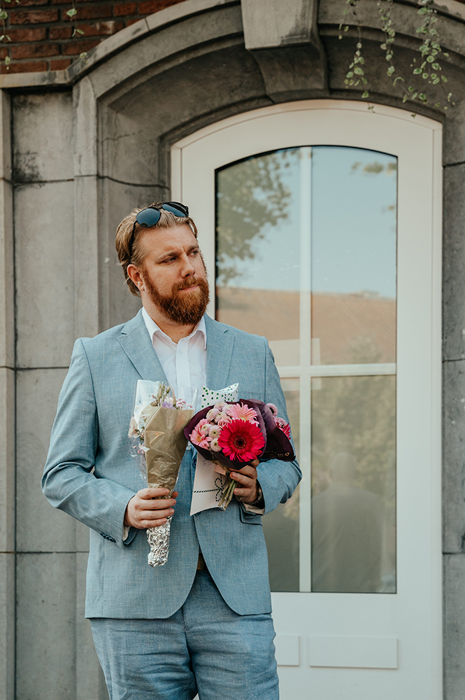 getuige van de bruiloft staat met alle geschonken bloemen in de hand het bruidspaar op te wachten-huwelijksfotografie-trouwreportage-byFotografils-IlseWagemakers-Fotograaf gevestigd in Essen