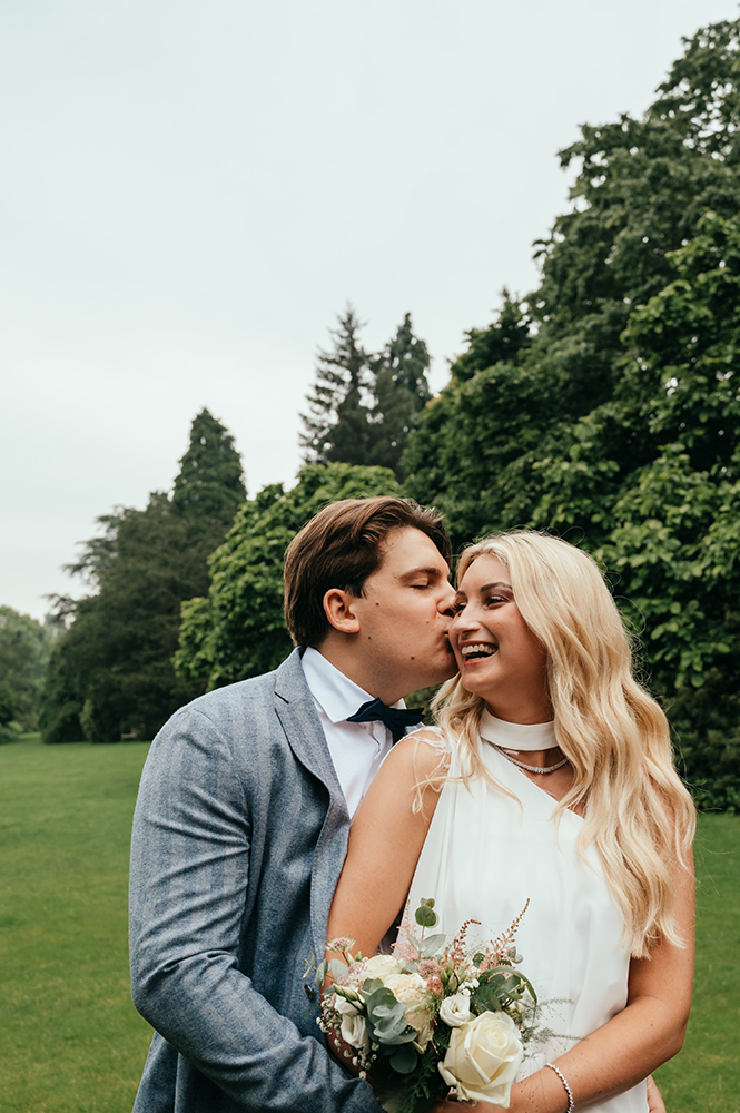 bruidegom kust bruid op de wang en omhelst haar-huwelijksfotografie-trouwreportage-byFotografils-IlseWagemakers-Fotograaf gevestigd in Essen