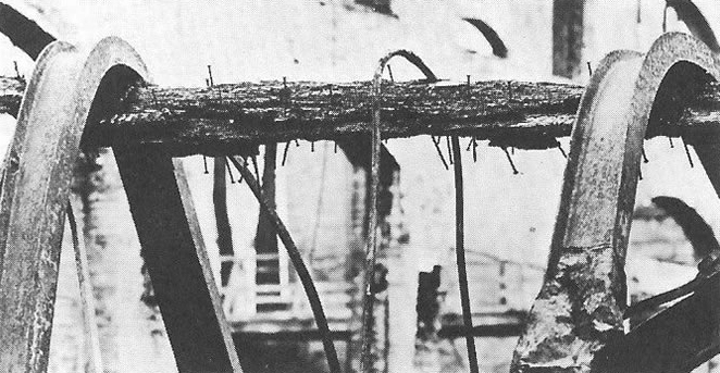 Scena post-incendio: Si vede una trave in legno supportare due travi in acciaio collassate.