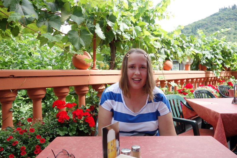 Eine Frau sitzt lächelnd auf einer Terrasse mit Blick auf die Umgebung