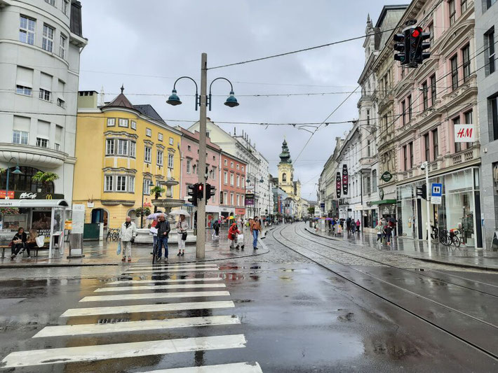 Blick in die Linzer Landstraße mit Straßenbahnschienen und historischen Fassaden bei Regen