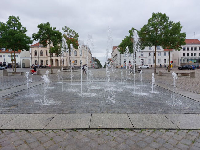 Die Wasserspiele auf dem zentralen Marktplatz von Neustrelitz vor der Kulisse klassizistischer Gebäude