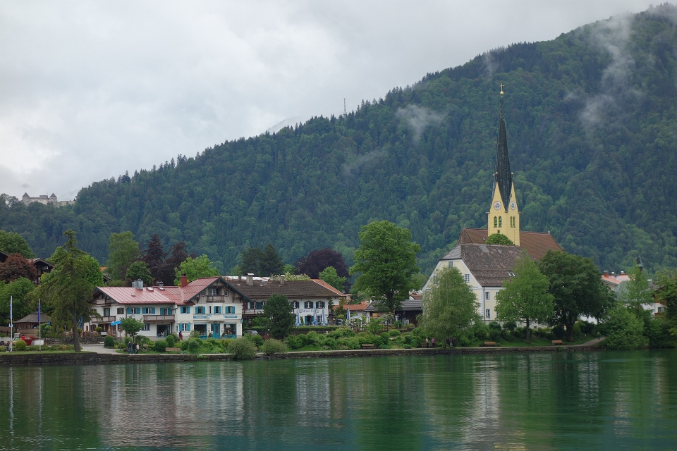 Blick über den Tegernsee auf die markante Kirche von Gmund unter bewölktem Himmel