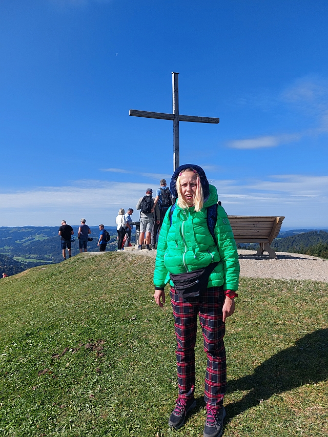 Christina steht stolz am Gipfelkreuz des Hündle mit Blick ins Tal
