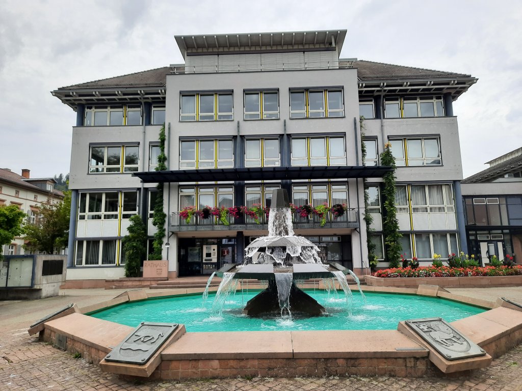 Ein moderneres, größeres Gebäude (vielleicht das Rathaus) mit einem Wasserspiel davor