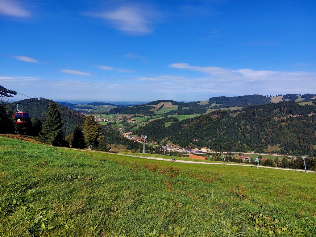 Weite Sicht über grüne Almen und bewaldete Hügel unter einem strahlend blauen Himmel