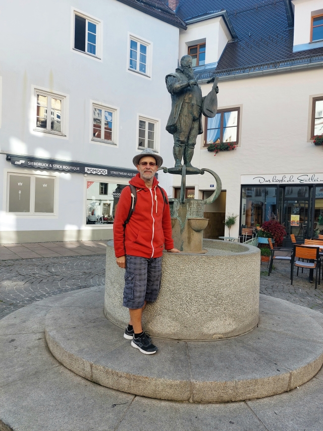 Andreas steht vor einem Brunnen auf einem belebten Platz in Füssen