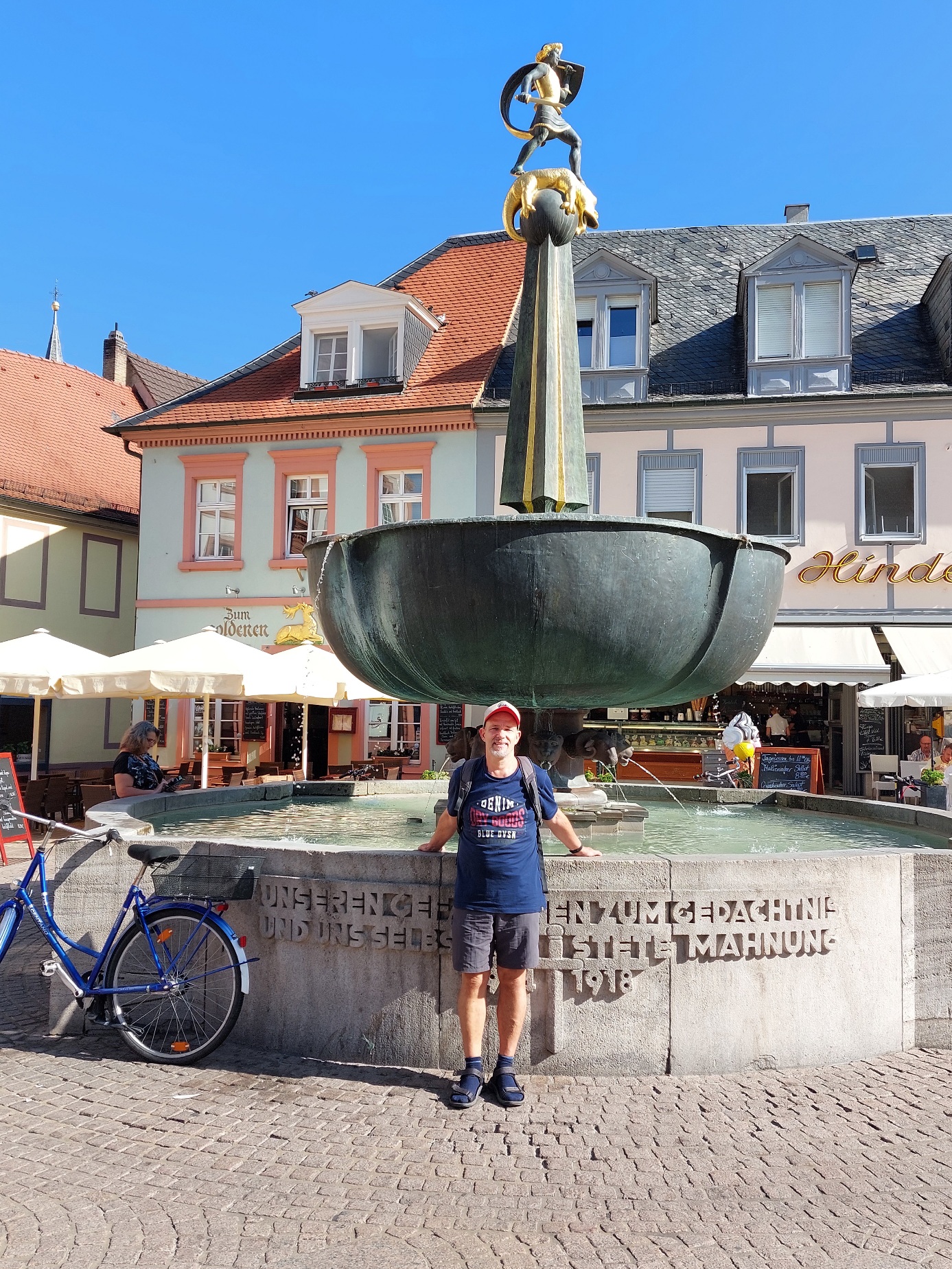 Ein historischer Brunnen in der belebten Maximilianstraße mit Blick auf die Cafés