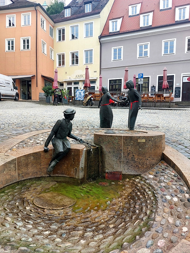 Ansicht eines gepflasterten Platzes mit Brunnen und Blick auf die umliegende Architektur