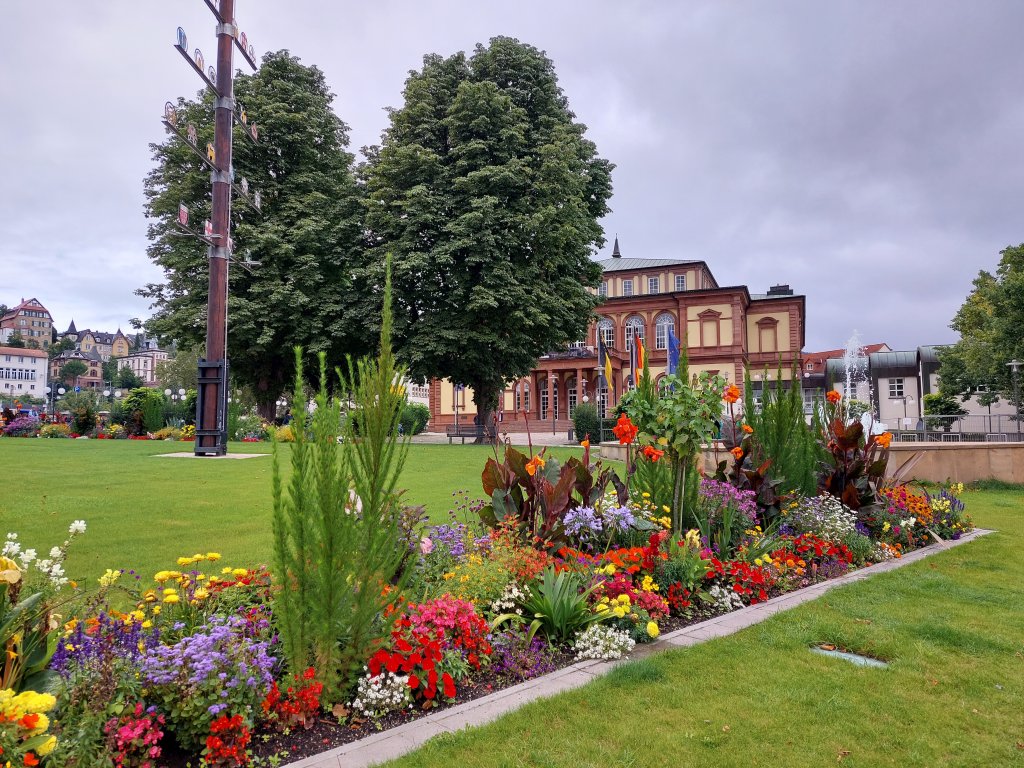 Ein herrlich angelegtes, buntes Blumenbeet im Stadtpark von Neustadt an der Weinstraße vor einem historischen Gebäude
