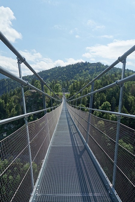 Blick direkt über den Gitterrost der Hängebrücke in Richtung der bewaldeten Berge