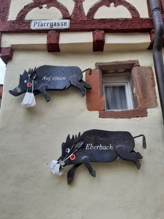 Zwei schwarze Eber-Figuren an einer Hauswand in der Pfarrgasse, die während der Corona-Zeit Stoffmasken tragen
