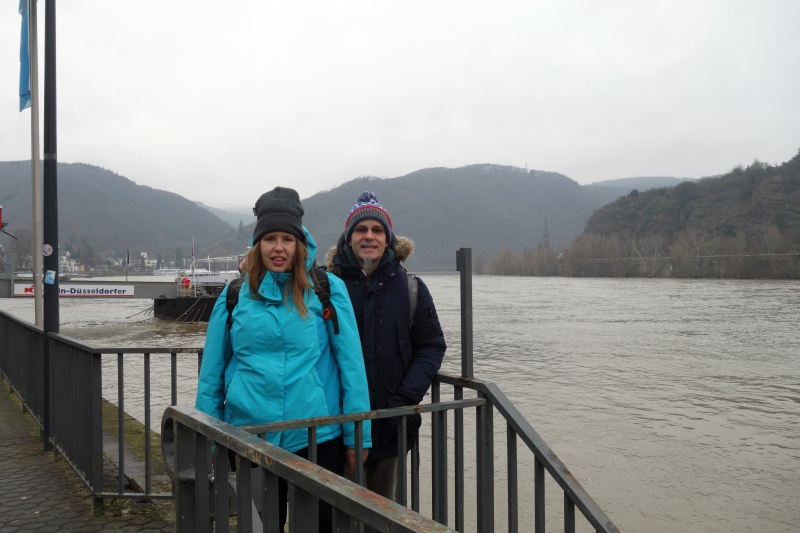 Andreas und Christina lächeln vor dem winterlichen Panorama des Rheins während ihres Spaziergangs