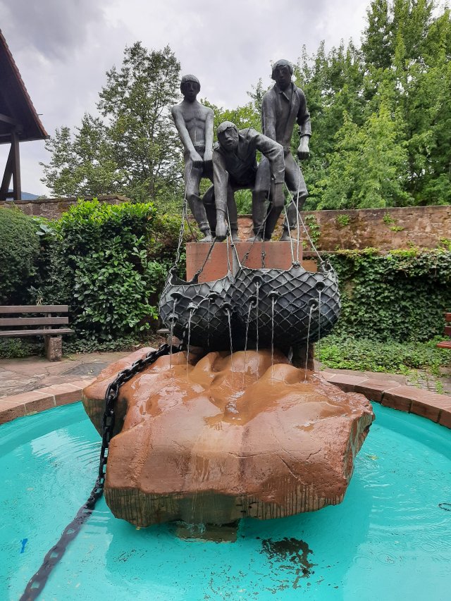Ein Brunnen mit einer Eber-Skulptur in der Mitte, umgeben von gepflegten Grünanlagen