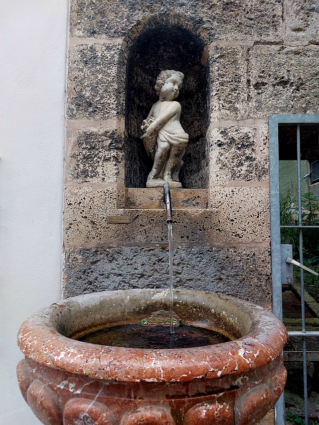 Detailaufnahme eines antiken Wandbrunnens mit einer kleinen Steinstatue in einer Nische