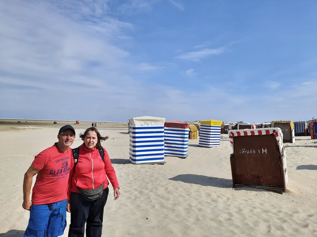 Zwei Personen spazieren entlang der bunten Strandzelte im Sand