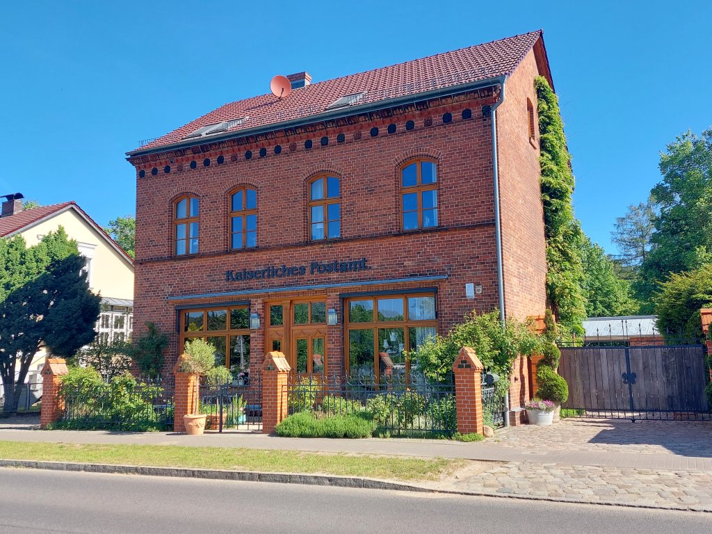 Das historische Kaiserliche Postamt in Biesenthal, ein zweistöckiger Backsteinbau mit großen Rundbogenfenstern und gepflegtem Vorgarten