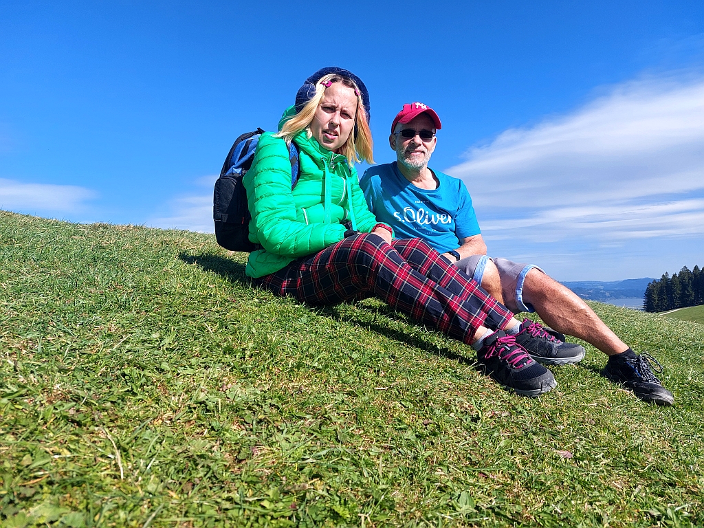 Andreas und Christina sitzen entspannt im Gras und genießen die Aussicht auf die Berge