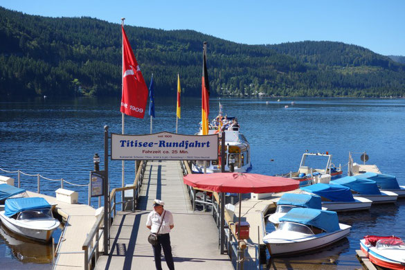 Blick auf den hölzernen Anlegesteg für die Titisee-Rundfahrt mit mehreren bereitliegenden Motorbooten und Segelbooten
