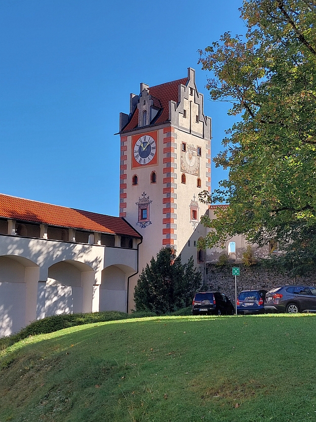 Blick über eine grüne Wiese auf die Türme der Füssener Kirchen und das Schloss