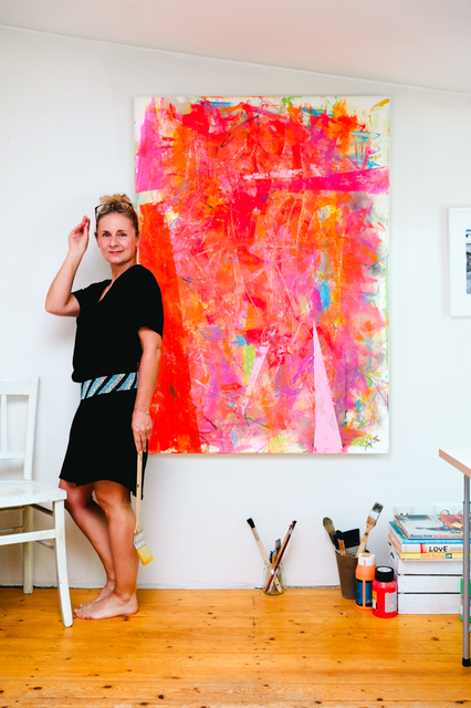 Die Künstlerin Annette Sandt steht vor einem ihrer lebendigen Werke, umgeben von knalligen Farben und pulsierender Energie.