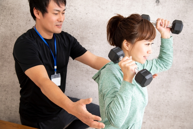 トレーナーに教わりながら運動している女性