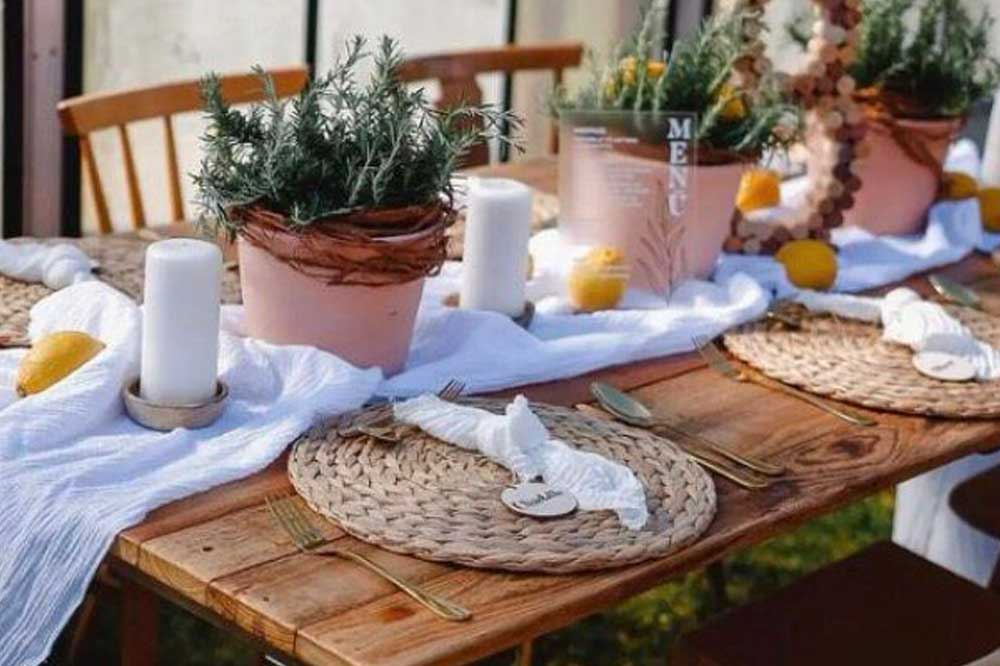 Hochzeit in einer alten Gärtnerei. In einem Gewächshaus ist ein überlanger Holztisch aus alten Scheunenbretter mit Haipinfüße aufgebaut mit Vintage Stühlen und runden Vintage Kissen bestückt.