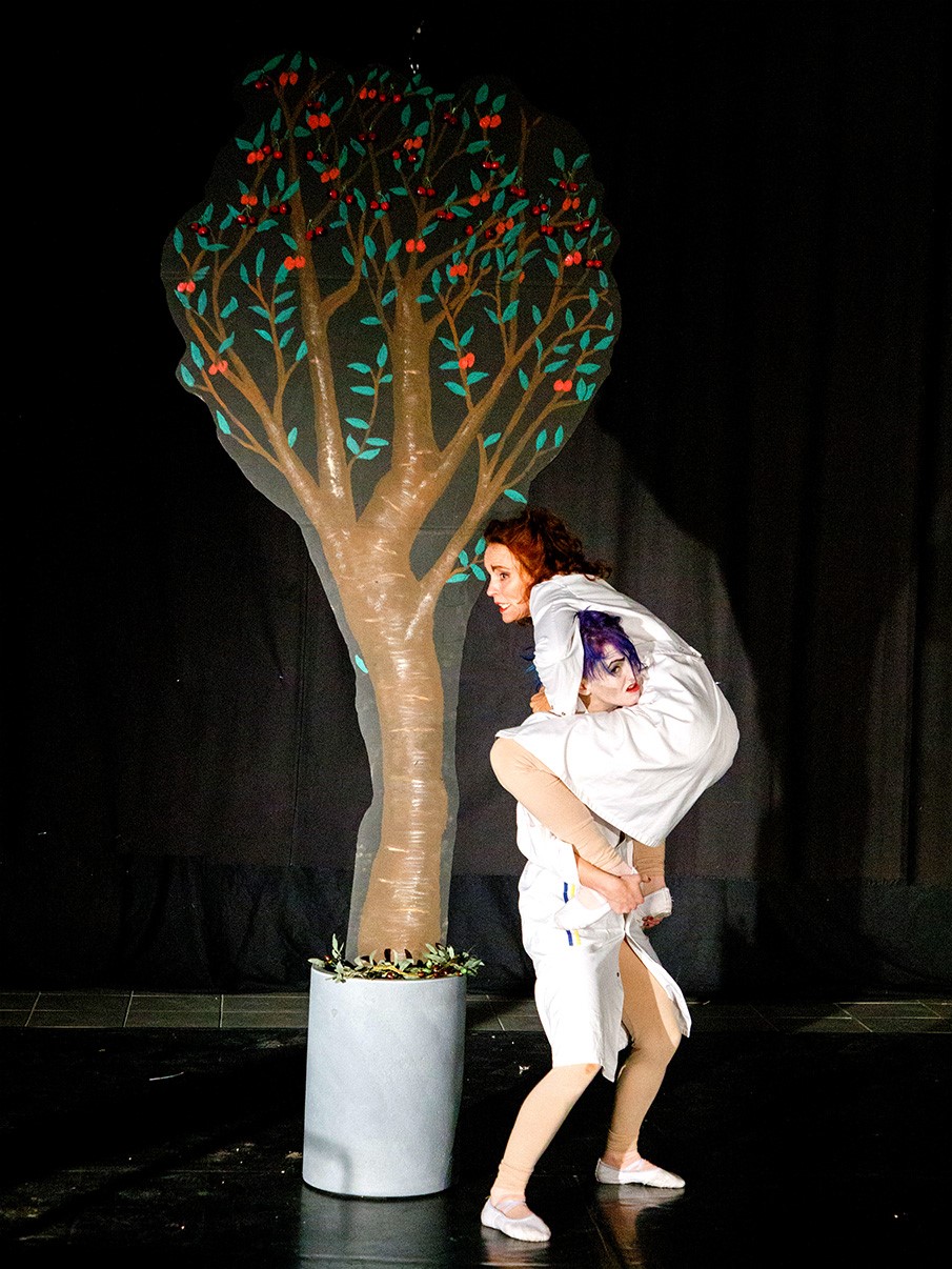 Theater: Eine Frau steht auf einer anderen vor einem Kirschbaum