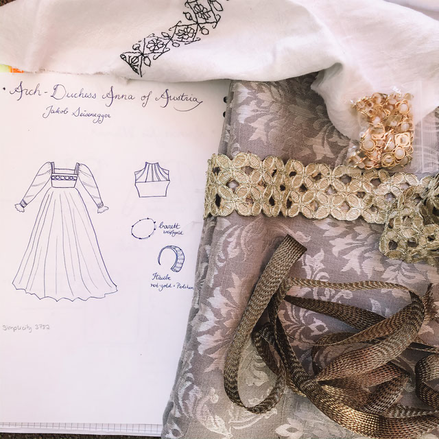 Detailfoto Zeichenblock mit Renaissancekleid-Zeichnung, Stoffen und Borten, bereit für Kostümschneidereiprojekt