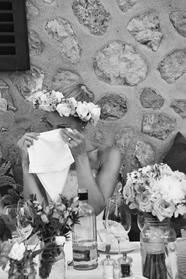 Braut mit Blumenkranz sitzt emotional am Hochzeitstisch und trocknet sich Tränen ab