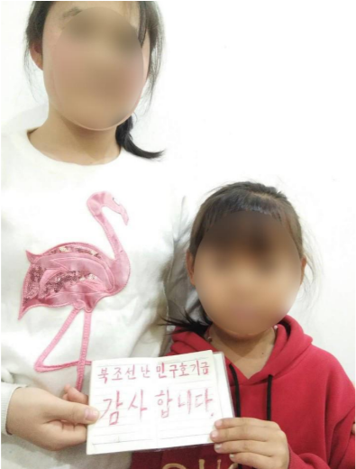 手に「北朝鮮難民救援基金　ありがとう」と書かれた紙を持つヒャニとシニ (サモは別室にいたため写っていない)
