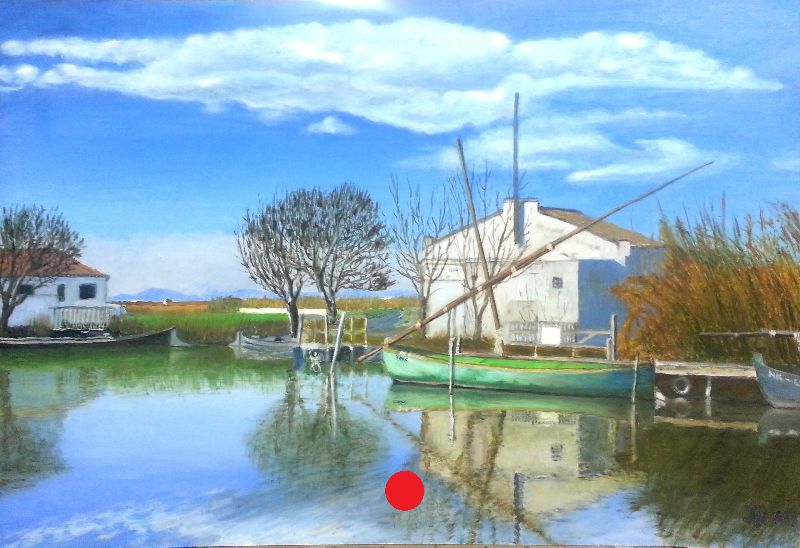 Barcas amarradas junto a casas blancas del puerto de El Palmar, con reflejos nítidos en el agua y cielo azul con nubes.