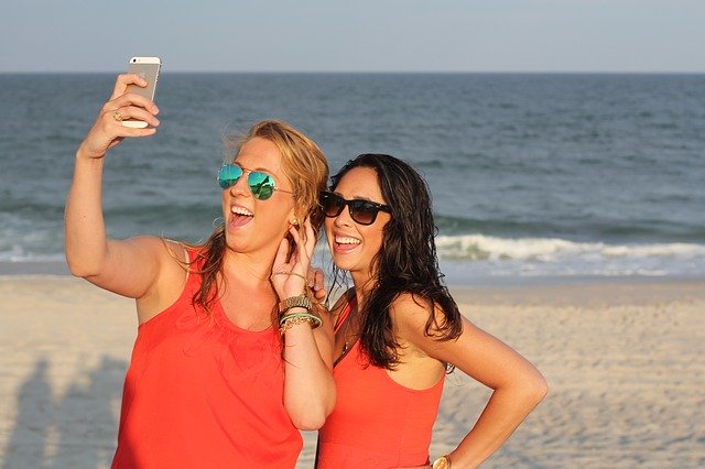 Zwei junge Frauen Teenager am Strand mit Handy beim Selfie machen.