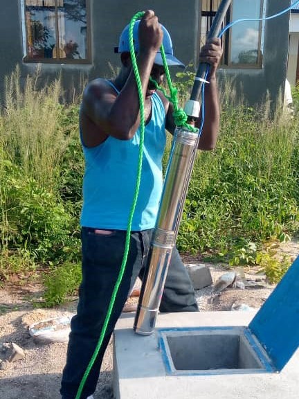 Ein Handwerker versenkt die Pumpe im Brunnen.