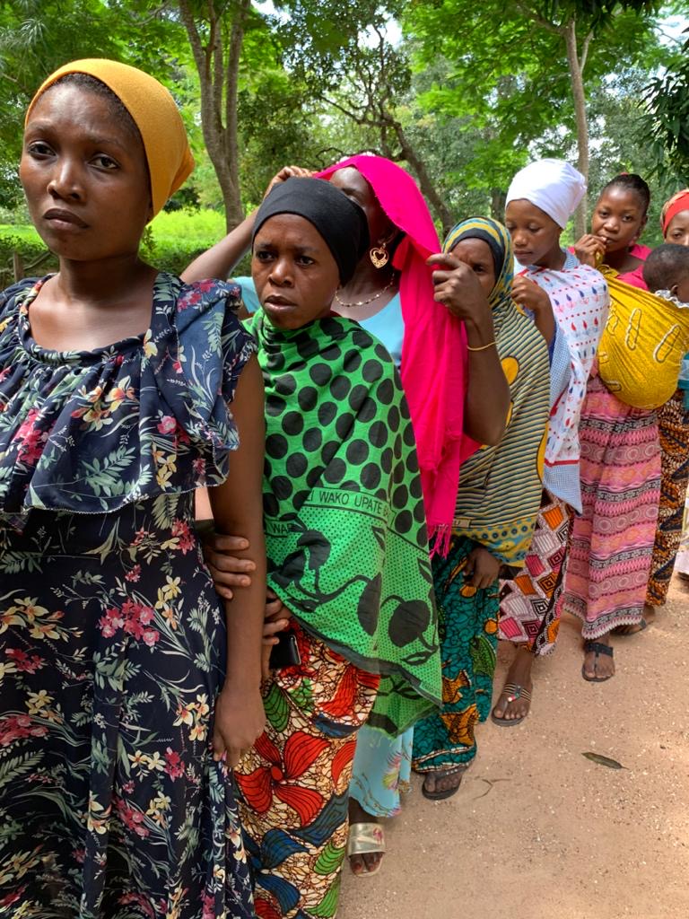 Frauen in farbenfroher afrikanischer Kleidung warten in einer Schlange auf Unterstützung – Kinder auf dem Rücken