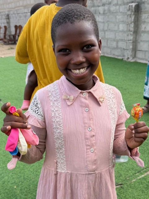 Kleines Mädchen in rose Kleid lächelt und hat Luftballons und Süßigkeiten in der Hand.