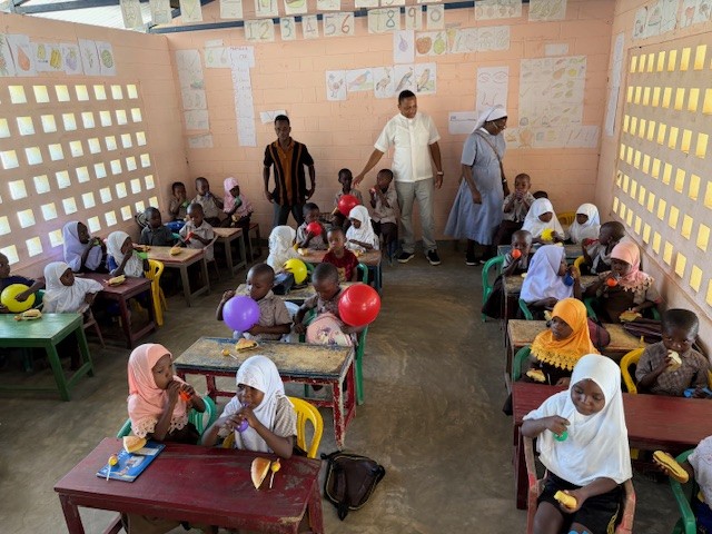 Volles Klassenzimmer mit jungen Kindergarrtenkindern und Sr Clementina, dem neue Pfarrer David und Lehrer Fahadi.