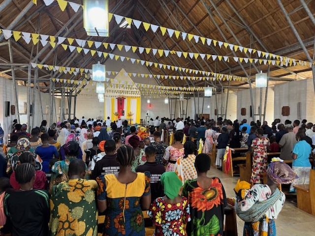 Gottesdienst in einer Kirche die mit Wimpeln geschmückt ist. Die Anwesenden sind in bunte Kleidung gehüllt.