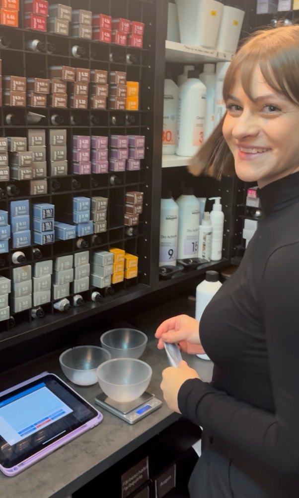 Eine freundlich lächelnde Friseurin wellt die Haare einer Kundin mit einem Glätteisen